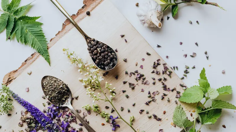 Herbes aromatiques séchées dans une cuillère, fleurs violettes et feuilles fraîches sur une planche en bois