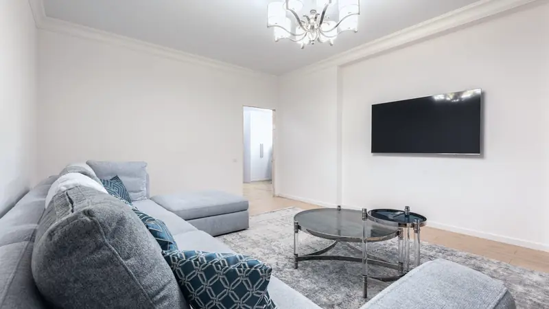 Salon clair avec canapé gris, table basse en verre et téléviseur éteint fixé au mur