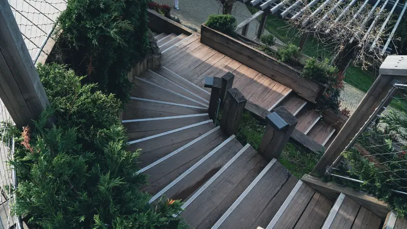 Escalier extérieur en bois à quart tournant dans un jardin, marches à nez antidérapants métalliques entre des conifères
