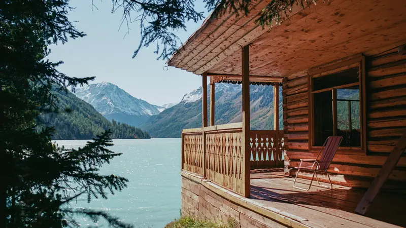Véranda d'un chalet en rondins au bord d'un lac de montagne, fermée par une balustrade en planches de bois découpées