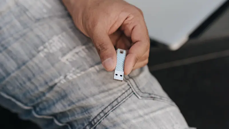 Main tenant une petite clé USB argentée au-dessus d'un genou en jean