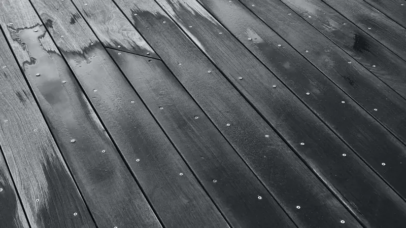 Lames de terrasse mouillées fixées par des vis inox apparentes, photographie en noir et blanc