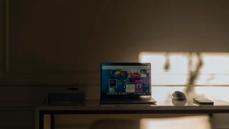 Ordinateur portable ouvert sur un bureau, à côté d'une souris et d'un smartphone, dans la lumière d'une fenêtre
