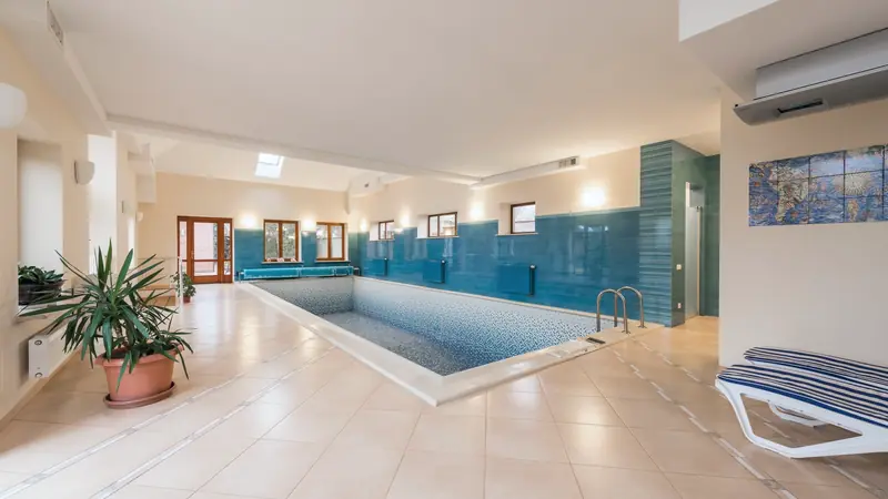 Piscine intérieure rectangulaire en mosaïque bleue avec échelle inox, sol carrelé beige et transat rayé