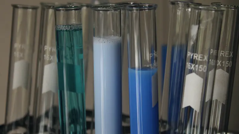 Tubes à essai en verre contenant des solutions bleues et turquoise, alignés sur un portoir de laboratoire