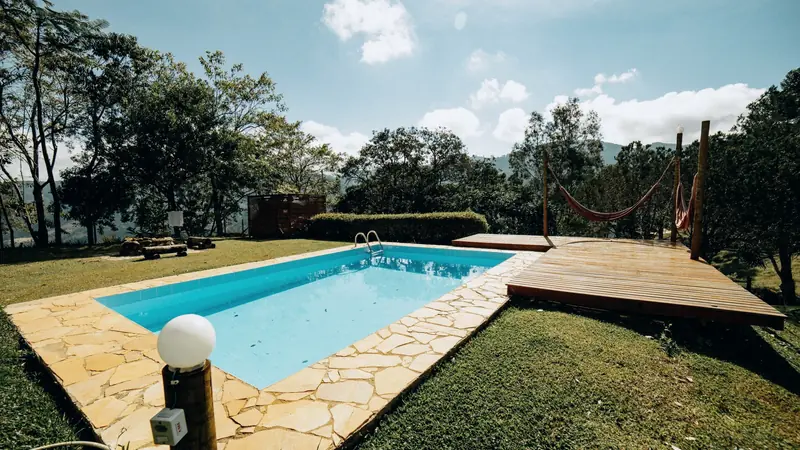 Piscine enterrée rectangulaire à l'eau bleue, entourée d'un dallage en pierre naturelle, d'une pelouse et d'une terrasse en bois