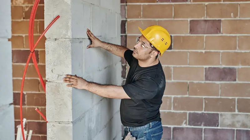 Ouvrier casqué vérifiant l'aplomb d'un mur en blocs de béton sur un chantier