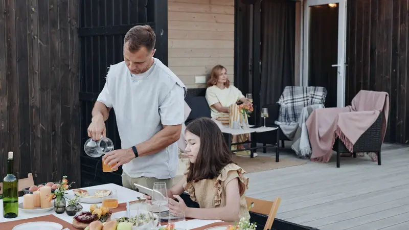 Terrasse en lames de bois gris légèrement surélevée devant une maison à bardage sombre, avec une table dressée au premier plan
