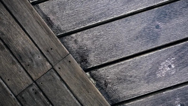 Lames de terrasse en bois patinées par les intempéries, vues de près, avec un cadre de lames posées perpendiculairement