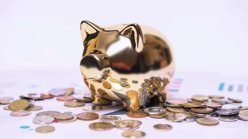 Tirelire dorée en forme de cochon entourée de pièces de monnaie éparpillées