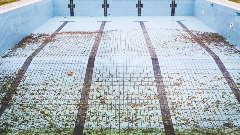 Bassin carrelé vidé, au fond couvert de feuilles mortes, avec des ouvertures rectangulaires en haut des parois