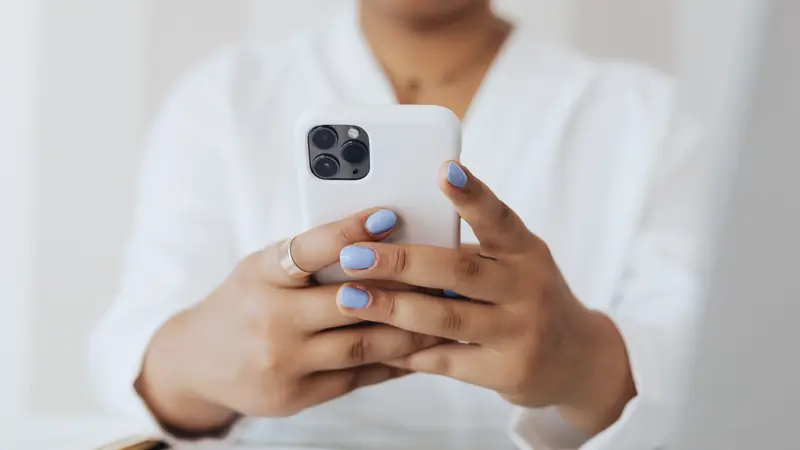 Personne en chemisier blanc tenant un smartphone à deux mains au-dessus d'un bureau