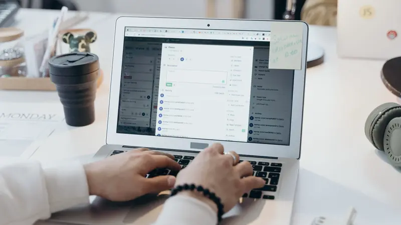 Mains tapant sur le clavier d'un ordinateur portable ouvert sur une application web, à côté d'un gobelet noir