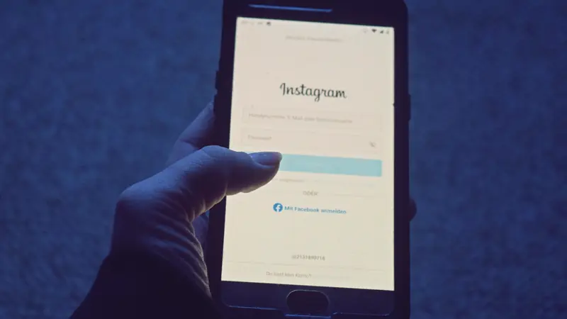 Main tenant un smartphone affichant l'écran de connexion d'Instagram, dans une lumière bleutée