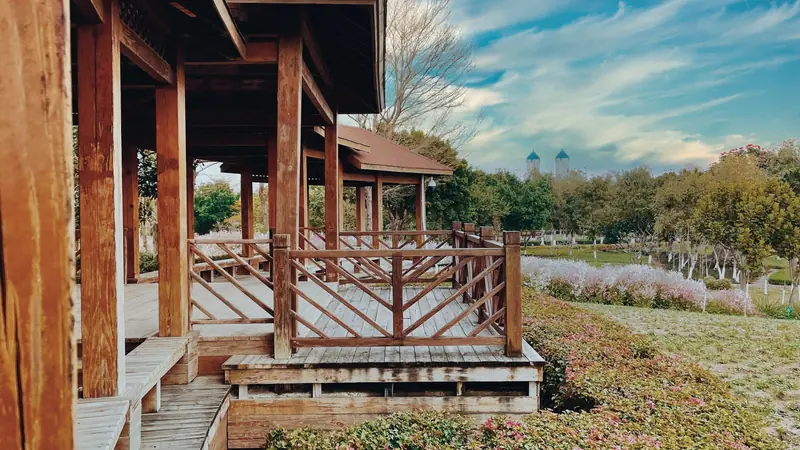 Plancher en bois surélevé bordé d'un garde-corps en bois, devant un pavillon dans un parc fleuri
