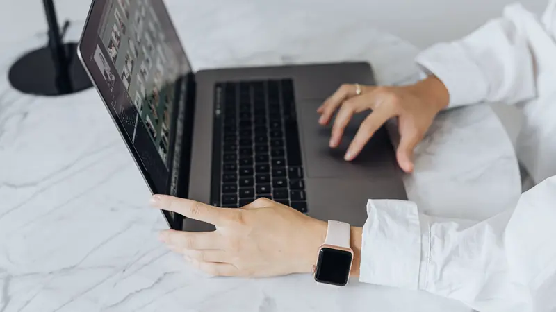Mains posées sur le pavé tactile et l'écran d'un ordinateur portable gris sur une table en marbre blanc