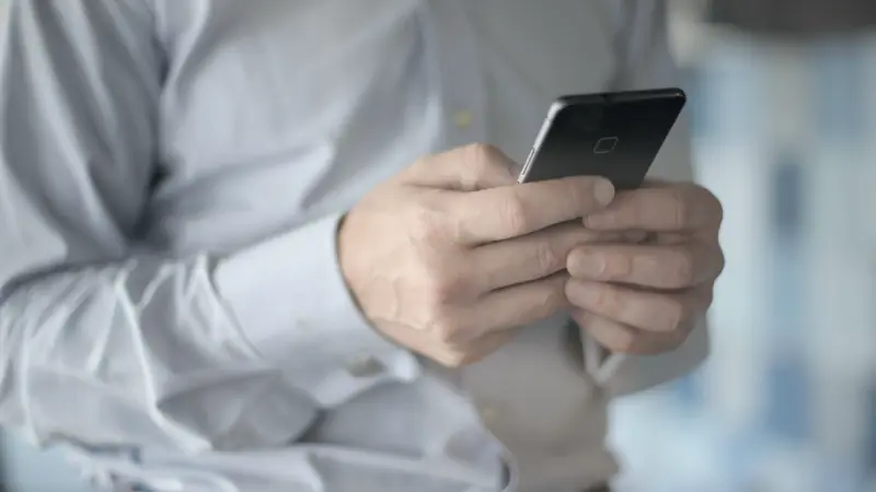 Homme en chemise claire tenant un smartphone à deux mains